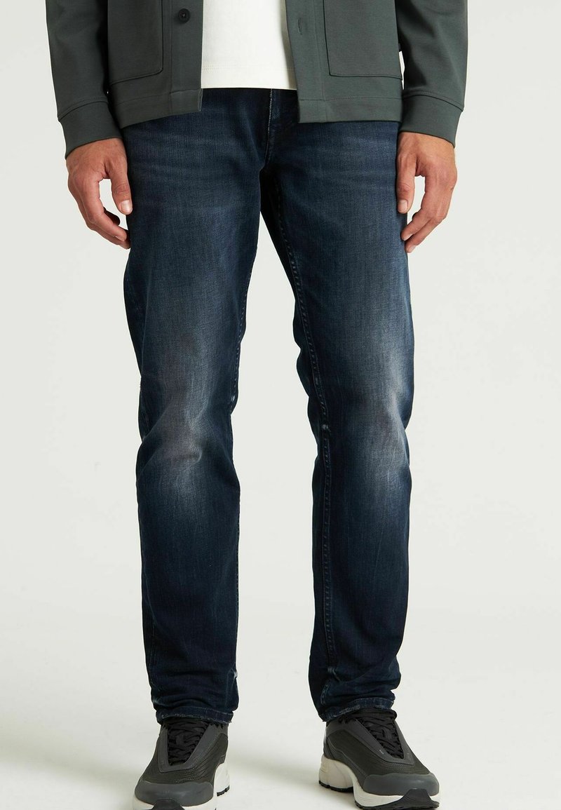 Temno modri jeansi iz denima z lahkim zbledelostjo, slim fit zasnova in standardni pet žepni stil, v kombinaciji s sivimi športnimi čevlji.