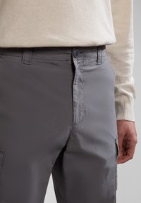 Pantaloni cargo grigi realizzati in tessuto leggero, con tasche laterali, chiusura a bottone e una superficie liscia, leggermente strutturata.