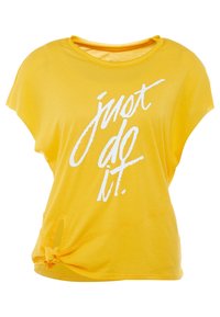Camiseta amarilla de manga corta hecha de una tela suave. Presenta un acento anudado en el lateral y un texto blanco que dice "solo hazlo".