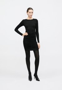 Μακρυμάνικο μαύρο φόρεμα με εφαρμοστή γραμμή, με ραβδώσεις στο ύψος της μέσης. Συνδυασμένο με διαφανές μαύρο καλσόν και μαύρες μυτερές γόβες.