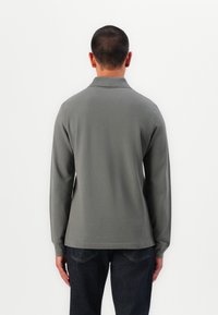 Graues Langarmpolohemd mit Kragen, aus strukturiertem Stoff. Das Hemd hat einen geraden Schnitt und wird mit dunklen Denim-Jeans kombiniert.