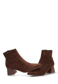 Botines de ante marrón con puntera puntiaguda y tacón ancho. Cuentan con cierre de cremallera y detalles sutiles de herrajes.