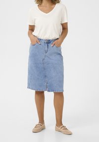 Džínová sukně, světle modrá, ke kolenům, s předními kapsami, zapínáním na knoflíky a rovným střihem s jemnými švy. Nosená s béžovým topem.