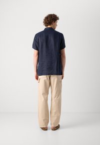 Donkerblauw linnen overhemd met korte mouwen en een rechte snit, gecombineerd met losse beige katoenen broek met zijzakken.