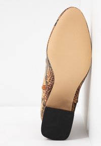 Semelle d'une chaussure à bout pointu avec une tige en motif peau de serpent et un talon carré noir, posée sur un fond blanc.