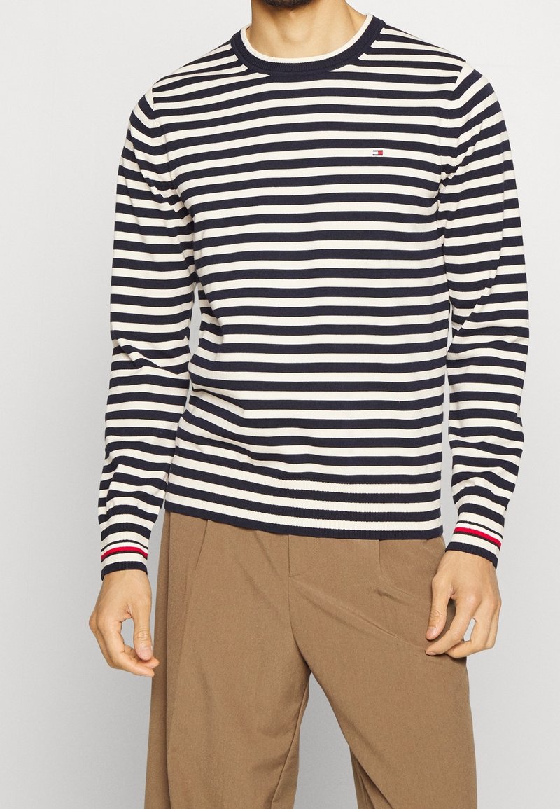 Marineblauw en crèmekleurig gestreept shirt met lange mouwen en een ronde halslijn, met een klein logo en een rode accenten op de manchetten. Zachte stofstructuur.