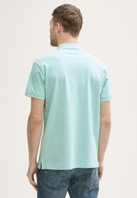 Mintgrünes Poloshirt mit kurzen Ärmeln, das eine dezente Textur und einen kontrastierenden Saum am Kragen und an den Ärmeln aufweist. Rückansicht sichtbar.