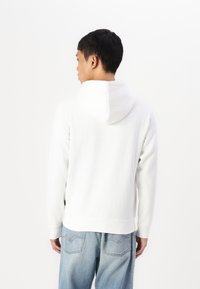 Witte katoenen hoodie met een kenguruzak en een verstelbare trekkoordkap, gecombineerd met lichtblauwe relaxed-fit jeans.