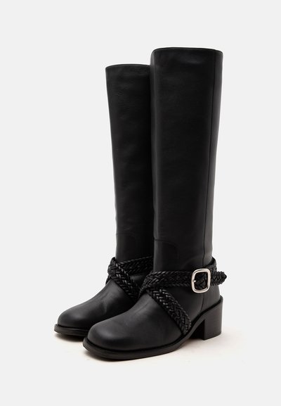 Paire de bottes hautes en cuir noir avec des lanières tressées et un détail de boucle argentée autour de la cheville, talons blocs et bouts arrondis.