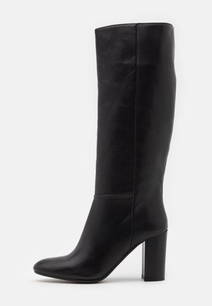 Botte noire en cuir montant jusqu'au genou, avec un bout arrondi et un talon bloc haut, vue de profil sur un fond uni.