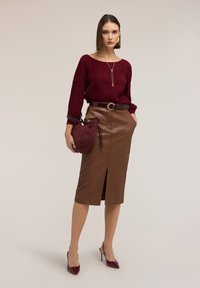 Bordeaux geribbelde trui, bruine leren kokerrok met vooraan een split, een getailleerde taille met een riem, en een kleine bordeauxrode tas. Rode puntige hakken.