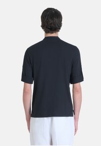 T-shirt nera a maniche corte con risvolti, realizzata in un tessuto morbido. Presenta un orlo dritto e fessure laterali per facilitare i movimenti.