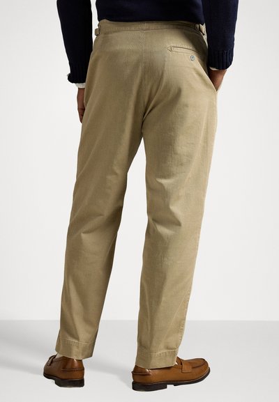 Chinos beiges à coupe droite, avec des détails de poche arrière. Fins à l'ourlet, portés avec des chaussures en cuir marron.