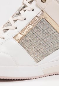 Vita sneakers med en texturerad, flerfärgad mesh-panel och metalliska guldaccenter; inkluderar ljusbeiga snören och en gummisula.