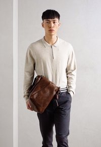 Khaki pullover met een ritskraag, gecombineerd met donkere broek en een grote bruine leren schoudertas, met afgeronde randen en een gestructureerd oppervlak.