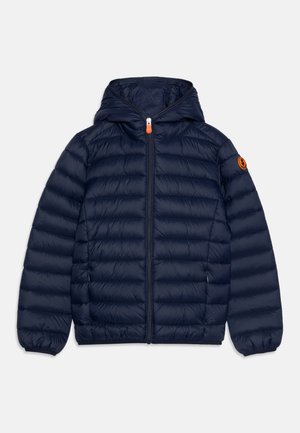 Veste matelassée bleu marine à capuche avec fermeture éclair à l'avant, deux poches latérales, poignets élastiques et un patch logo orange sur la manche gauche.