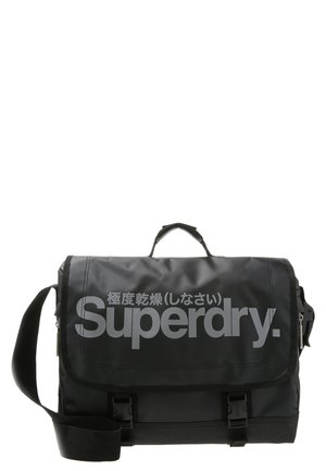 Czarna torba listonoszka z regulowanym paskiem na ramię, górnym uchwytem, przednią klapą z logo "Superdry" i japońskimi znakami w kolorze szarym.