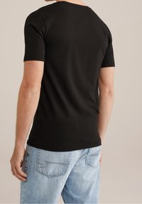 T-shirt nera in cotone con maniche corte e scollatura rotonda, vista da dietro. Abbinata a jeans in denim blu chiaro.