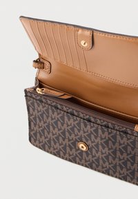 Ruskea kuvioitu lompakko, jossa on MK-logo, sileä vaaleanruskea nahkasisusta korttipaikkoineen, vetoketjullinen osio ja painonappisuljenta.