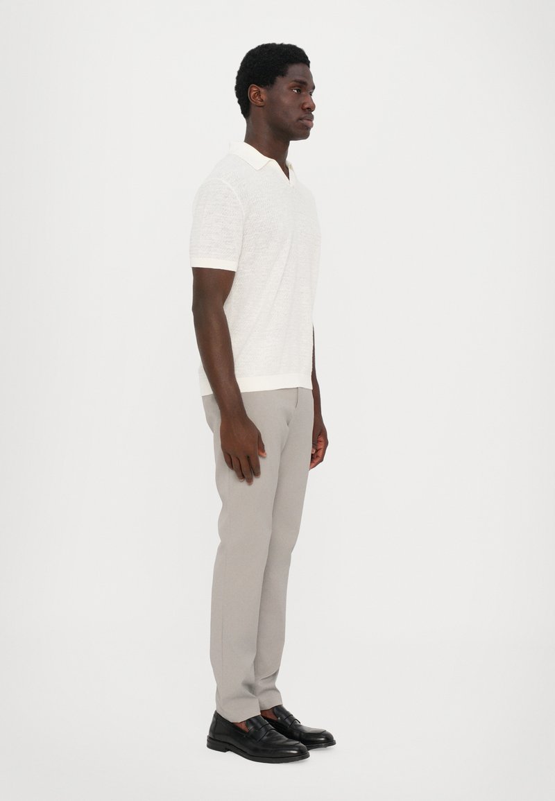 Short-sleeve, textured white polo with a contrasting collar, paired with light gray tailored pants and black shoes. Side profile view.