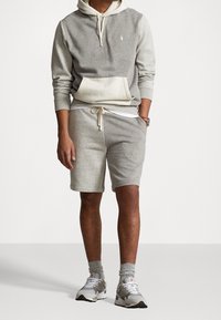 Ljusgrå hoodie med en framficka och snörning, matchad med kortbyxor. Bärs med grå sneakers och ribbade strumpor.