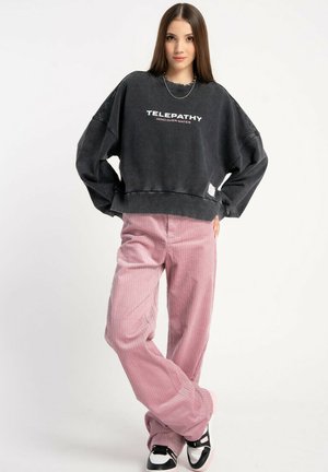 Czarny, oversize’owy sweatshirt z napisem "TELEPATIA MIND OVER MATTER" w białym kolorze, zestawiony z jasnoróżowymi, szerokimi spodniami z korduroyu.