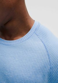 Helles blaues Sportshirt mit einem strukturierten, gepunkteten Muster und einem runden Halsausschnitt. Verfügt über glatte Nähte entlang der Säume.