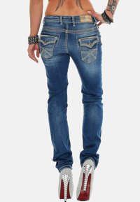 Jeans en denim bleu skinny avec des poches arrière décoratives, un léger décoloration et des coutures contrastées. Associés à des escarpins argentés à clous.