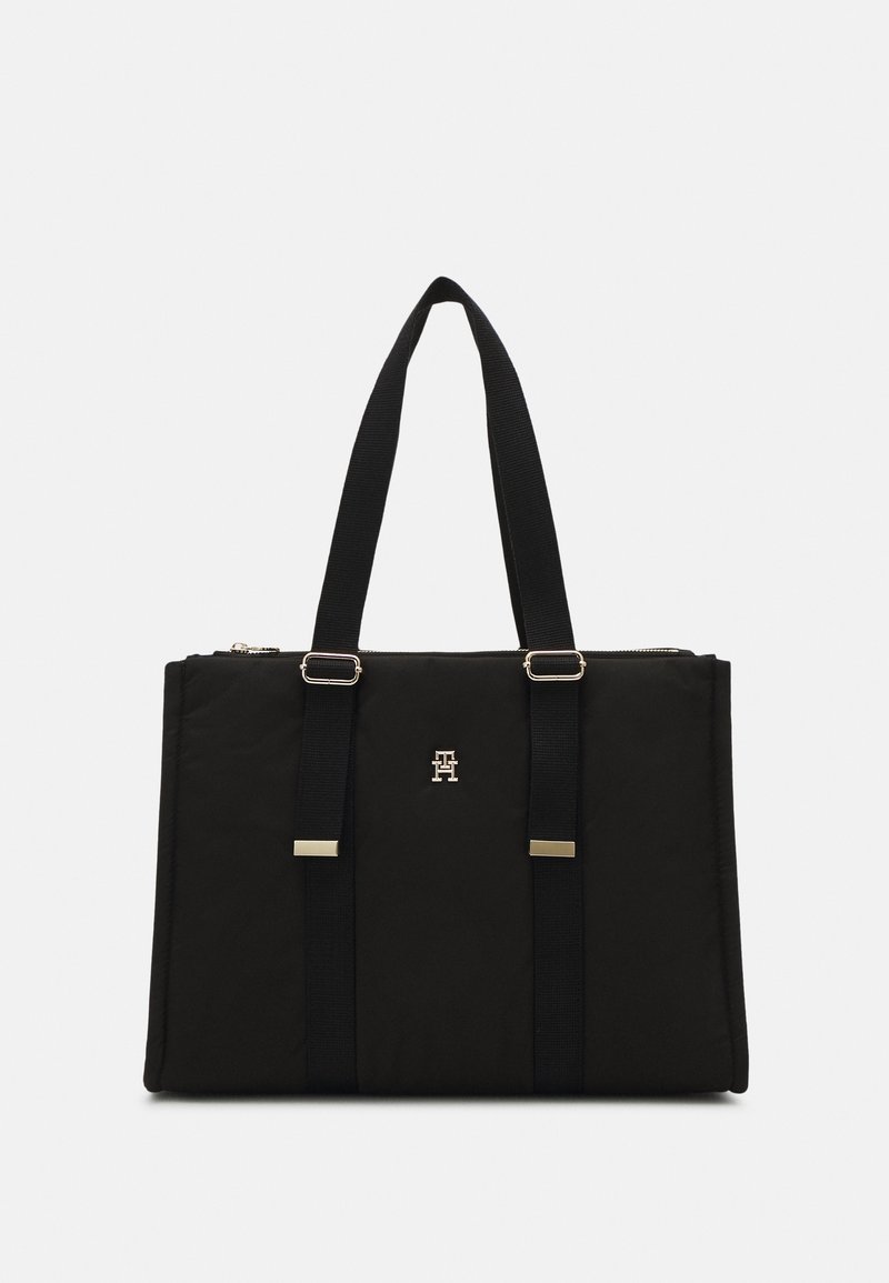 Sac cabas rectangulaire noir avec deux longues anses, détails en métal doré et petit logo métallique central à l’avant.