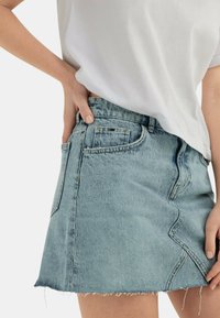 Gonna di jeans in blu chiaro con orlo sfilacciato, design aderente, tasca laterale e dettagli di cucitura in evidenza. Abbinata a una t-shirt bianca.