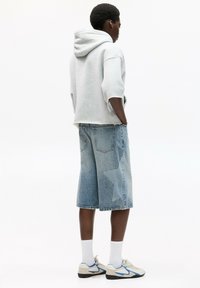 Sweatshirt à capuche gris, short en denim bleu clair avec un motif d'étoiles et baskets neutres avec des accents bleus. Des chaussettes blanches complètent la tenue.