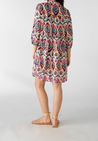 Vestido de manga corta con estampado en crema y diseño en rosa, verde y azul; presenta un corte holgado y hasta la rodilla, combinado con sandalias beige.