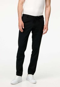 Pantaloni neri dal design elegante, con vita regolabile, gambe affusolate e una consistenza del tessuto liscia. Indossati con sneakers bianche.