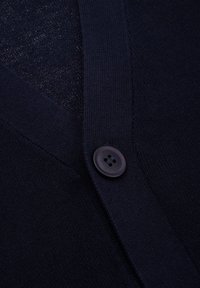 Granatowy kardigan z dekoltem w serek, gładką fakturą i ciemnym guzikiem z czterema otworami. Materiał ma delikatny połysk.