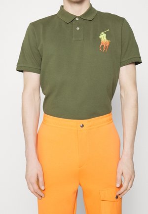 Groen poloshirt met kraag en twee knopen, met een neongele en oranje geborduurd logo. Gecombineerd met oranje broek.