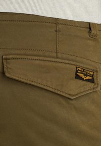 Pantalons verts olive avec une poche arrière arborant une étiquette PME Legend noire et jaune, fabriqués à partir d'un tissu lisse et durable.