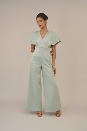 Mintgrüner Jumpsuit mit weitem Bein, V-Ausschnitt und ausgestellten Capesäulen. Glattes Material mit taillierter Struktur und minimalen Nähten. Goldene Sandalen.