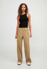 Top negro sin mangas con ribetes blancos, combinado con unos pantalones beige holgados. El conjunto presenta una cinturilla elástica y un diseño minimalista.