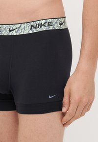 Black cotton boxer shorts featuring a textured mint green waistband with "NIKE" branding and a small grey logo on the thigh.