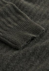 Ciemnozielony, teksturowany materiał wełniany z prążkowanym wzorem, prezentujący miękkie włókna i gruby, ciepły wygląd. Krawędzie są nieobrobione.