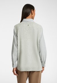 Lichtgrijze gebreide vest met een kraag, met lange gestreepte mouwen in blauw en wit. Inclusief accenten van knopen in goudkleur op de manchetten.