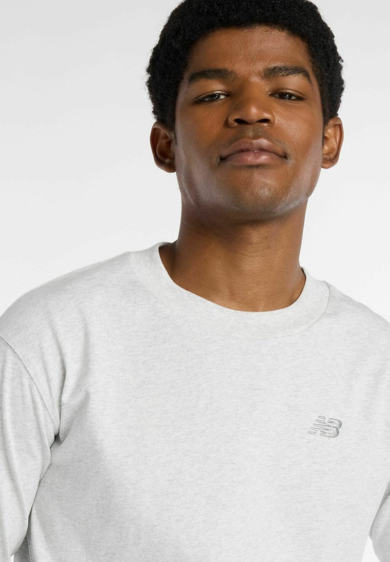 Light gray sweatshirt featuring a round neckline, soft texture, long sleeves, and a small embroidered logo on the chest.