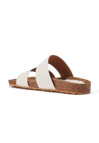White slide sandals with crisscross straps, cork footbed, and textured brown outsole. Soft lining visible above the footbed.