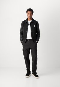 Sort jakke med læderærmer, hvid t-shirt med logo, sorte cargo bukser og sorte sneakers med hvide såler.