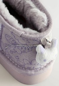 Lilla ruskindsstøvle med blødt faux fur-futter, der har en tekstureret overflade, blomsterdesign og en blød katteformet detalje på bagsiden.