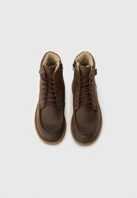 Brūnas ādas potītes zābaki ar teksturētu apdari, priekšpusē ar šņorēm, mākslīgās kažokādas oderējumu, sānu rāvējslēdzēja aizdari un kontrastējošu gumijas zolīti.