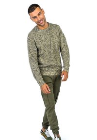 Maglione lavorato a maglia in un motivo testurizzato beige e verde, abbinato a pantaloni cargo oliva e sneakers bianco e nere. Look casual, maniche lunghe.