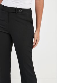 Zwarte broek met een gladde stoftextuur, een ritssluiting aan de voorkant, zijzakken en een getailleerde pasvorm met een rechte pootontwerp.