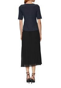 Donkerblauwe top met korte mouwen gecombineerd met een geplooide zwarte maxi rok en zwarte sandalen met bandjes, die een gladde stoftextuur en gelaagd ontwerp laat zien.