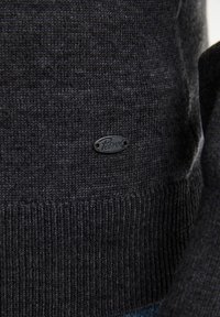 Pulover tricotat de culoare gri închis, cu un tiv ondulat și un mic logo negru. Textura materialului pare moale și uniformă.